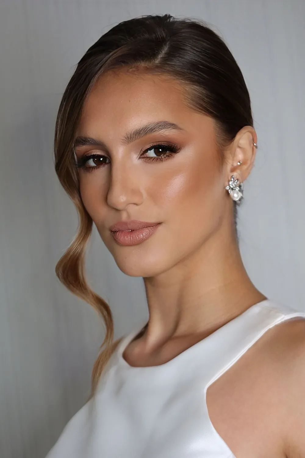 Mulher com cabelo preso e ondas soltas no rosto, olhos esfumados em tons terrosos e brincos delicados.