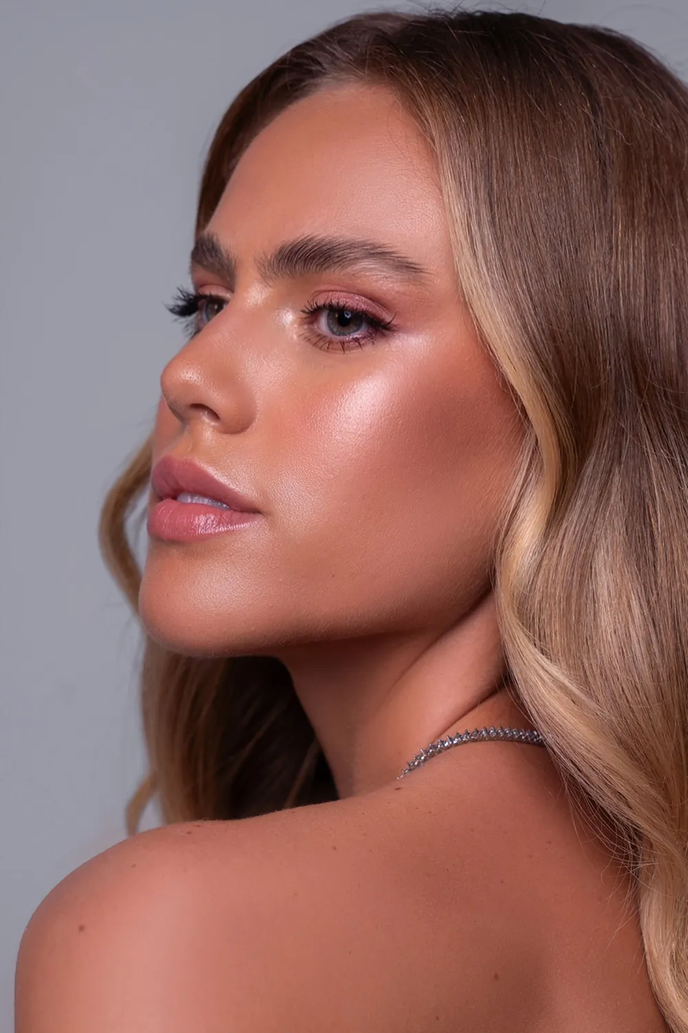Perfil de uma mulher de cabelos castanhos com pele luminosa, blush rosado e olhos esfumados suaves.